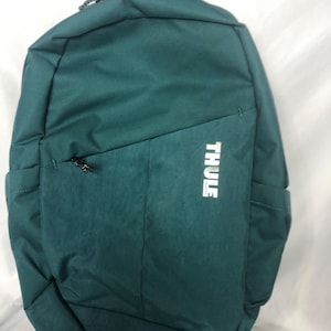May include: Teal backpack with a top handle and a zippered front pocket. The backpack has the brand name "THULE" printed in white on the front. The bag is made of a textured material.