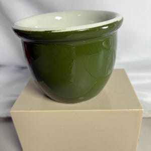 May include: A small, round ceramic bowl featuring a glossy, deep forest green exterior and a smooth, contrasting white interior. The bowl has a thick, rounded rim and a slightly tapered base, presenting a simple, functional design for serving.
