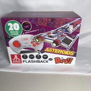 May include: A boxed Atari Flashback Blast! Vol. 2 video game console. The box is purple and white, with the words "20 Built-in Games" and "Asteroids" visible. A white controller with red buttons is shown on the front.