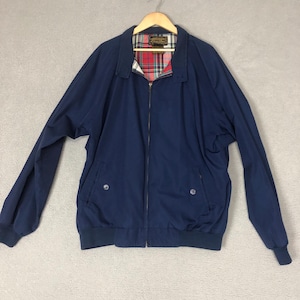 May include: A navy blue jacket with a full zipper closure and a classic collar. The jacket features two front pockets and a ribbed hem and cuffs. The interior lining has a red and green plaid pattern. The jacket is hanging on a wooden hanger.