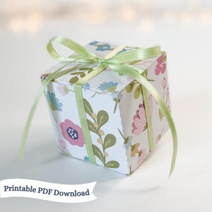 Peut inclure: Une petite boîte cadeau blanche avec un motif floral et un ruban vert. La boîte est nouée avec un nœud et le ruban est assez long pour pendre de la boîte. Le texte "Printable PDF Download" est en bas de l'image.
