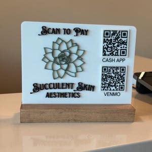 Könnte beinhalten: Ein weißes Acrylschild mit Holzsockel, das ein lasergeschnittenes Sukkulenten-Design und den Text "Scan to Pay" und "Succulent Skin Aesthetics" zeigt. Enthält QR-Codes für Cash App und Venmo.
