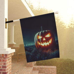 Może przedstawiać: Czarna flaga halloweenowa z podświetloną dynią z przerażającą twarzą. Dynia znajduje się na polu trawy z drzewami w tle.