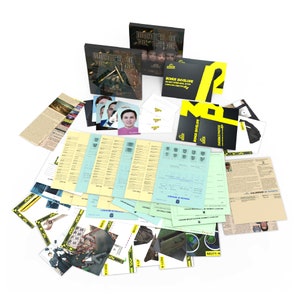 Puede incluir: Un juego de misterio de asesinato con una caja amarilla y negra, una caja negra y blanca y una variedad de documentos, incluido un calendario de eventos, sobres de evidencia y fotos. El juego se llama "Murder in the Office".