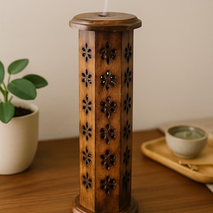 Könnte beinhalten: Ein dunkelbrauner ätherischer Öl Diffusor aus Holz mit einem floralen Muster, das in die Seiten geschnitzt ist. Der Diffusor gibt Dampf von oben ab. Er steht auf einer Holzoberfläche, was auf ein natürliches Wohn-Dekor-Thema hindeutet.