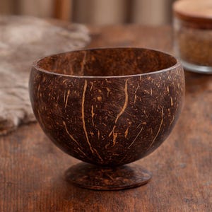 May include: A handcrafted coconut bowl with a pedestal base. The bowl is a rich brown colour with natural grain patterns and a smooth interior. This eco-friendly bowl is perfect for serving snacks or small portions.