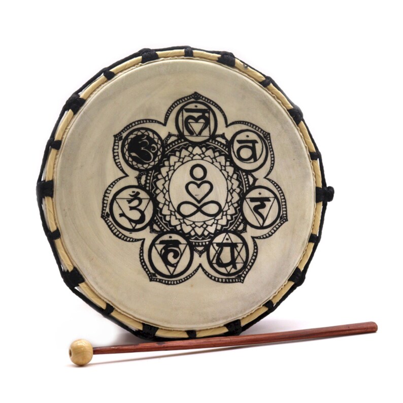 Op de afbeelding: Een ronde trommel met een natuurlijke huidkop, versierd met een zwart chakra-symboolontwerp. De trommel heeft een houten frame en wordt geleverd met een houten drumstok. Een muziekinstrument voor meditatie en spirituele praktijken.