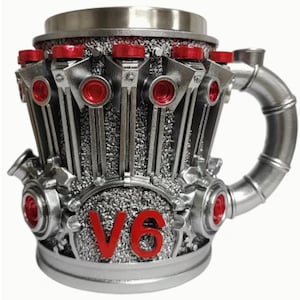 Puede incluir: Una taza de color plateado con un diseño de motor V6. La taza presenta detalles en rojo en los componentes del motor y el texto "V6" en rojo. El asa es un tubo metálico curvado.