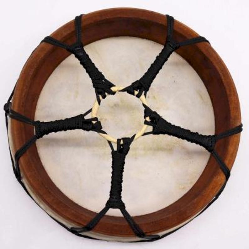 Op de afbeelding: Een ronde, handgemaakte trommel met een lichtgekleurd, gespannen huidoppervlak. Het houten frame van de trommel is donkerbruin en heeft een stervormig patroon van zwart touw over het oppervlak. Muziekinstrument.