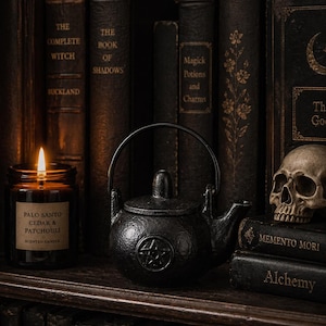 May include: A dark, atmospheric still life with a black cast iron teapot, a burning candle, and a skull. The scene includes old books with titles such as "The Book of Shadows" and "Magick Potions and Charms", creating a gothic aesthetic.