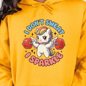 May include: A yellow hoodie featuring a graphic of a unicorn lifting weights. The text on the graphic reads "I don't sweat I sparkle".