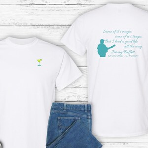 May include: Two white t-shirts, one with a margarita glass graphic and the other with a silhouette of a man playing a guitar and the text "Some of it's magic, some of it's tragic, But I had a good life all the way. Jimmy Buffett 12/25/1946 - 9/1/2023"