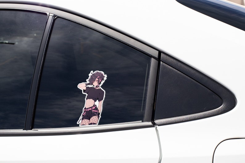 K&ouml;nnte beinhalten: Ein Aufkleber mit einem Anime-Charakter mit schwarzen Haaren, der ein schwarzes Crop-Top, rosa Shorts und Netzstr&uuml;mpfe tr&auml;gt. Der Aufkleber befindet sich an der Heckscheibe eines wei&szlig;en Autos.