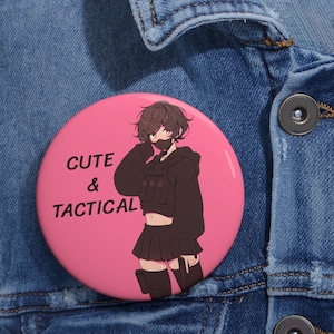 May include: A pink button with a cartoon illustration of a person wearing a black tactical vest and a black mask. The text "CUTE & TACTICAL" is printed on the button.