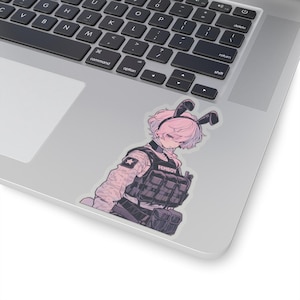 May include: A sticker featuring a cartoon illustration of a person with pink hair wearing a tactical vest and bunny ears. The person is looking down and the text "FEMBOY" is printed on the vest.