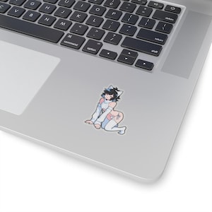 May include: A sticker depicting a cartoon character with black hair, cat ears, and a light blue and white outfit. The character is kneeling on a grey surface, with a stylized design on the thigh. The sticker is placed on a laptop.