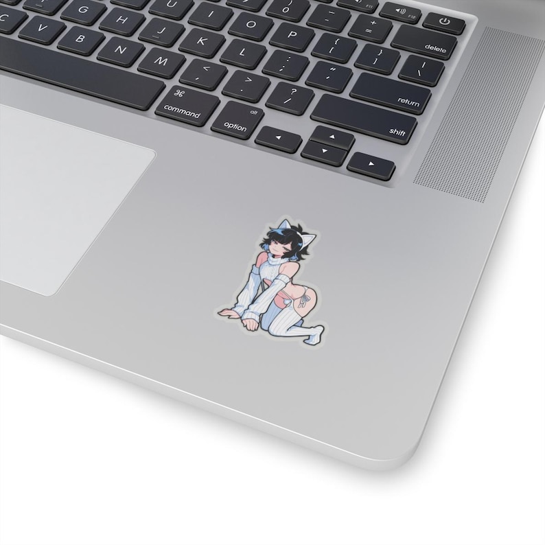 May include: A sticker depicting a cartoon character with black hair, cat ears, and a light blue and white outfit. The character is kneeling on a grey surface, with a stylized design on the thigh. The sticker is placed on a laptop.