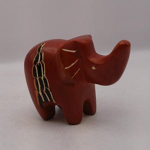 May include: A small, red, carved stone elephant figurine with black and white details. The elephant has a long trunk and is standing on all four legs.
