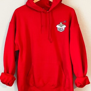 May include: Red hooded sweatshirt with a white graphic of a takeout container with noodles and chopsticks and the text "Send Noodles".