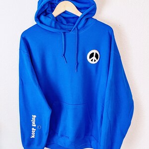 May include: A royal blue hoodie with a white peace sign patch on the front and the words "keep going" on the left sleeve.