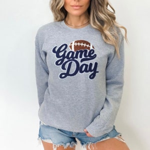 Peut inclure: Sweat-shirt gris avec un graphisme "Game Day" bleu marine et un graphisme de ballon de football marron.