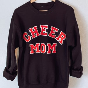May include: Black sweatshirt with red and white lettering that says "CHEER MOM".