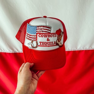 Puede incluir: Gorra de camionero roja, blanca y azul con una bandera estadounidense, una herradura, una bota de vaquero y el texto "Cowboys & Tequila".