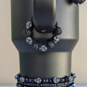 May include: Black beaded bracelets and a matching necklace with skull and round bead accents. The jewelry is displayed on a black tumbler. The bracelets have different bead styles and sizes.