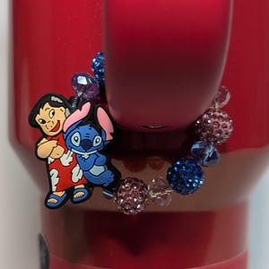 May include: A charm bracelet with a blue and pink beaded design. The charm features Stitch and Lilo from the Disney movie Lilo & Stitch.