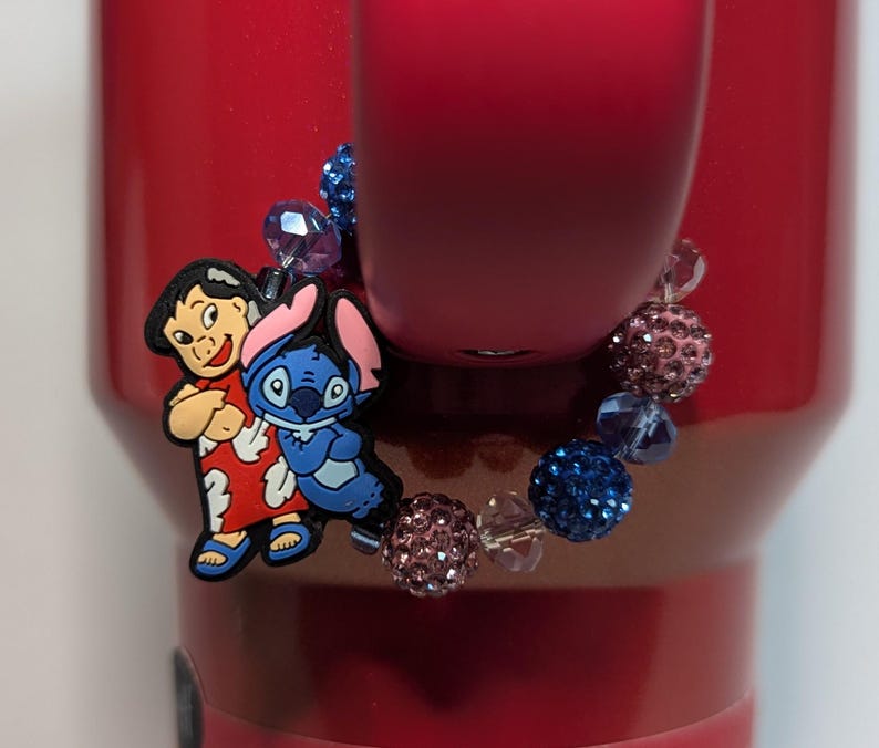 May include: A charm bracelet with a blue and pink beaded design. The charm features Stitch and Lilo from the Disney movie Lilo & Stitch.