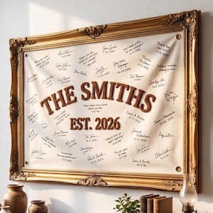 May include: A rectangular off-white fabric banner featuring the brown embroidered text THE SMITHS and EST. 2026, surrounded by numerous handwritten signatures and dates, displayed within an ornate, vintage-style gold-toned decorative frame.