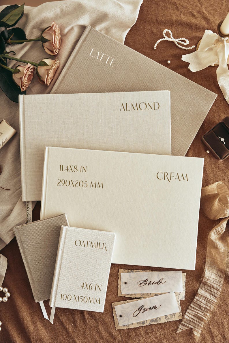 K&ouml;nnte beinhalten: Eine Auswahl an beigefarbenen und cremefarbenen Notizb&uuml;chern mit den Aufschriften "LATTE", "ALMOND", "CREAM" und "OATMILK". Die Notizb&uuml;cher haben verschiedene Gr&ouml;&szlig;en, darunter eines mit 290x205 mm. Ebenfalls enthalten sind zwei Tischkarten mit den W&ouml;rtern "Bride" und "Groom".