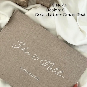 K&ouml;nnte beinhalten: Ein beiges Buch im A4-Format mit cremefarbenem Text, das die Namen "Zehra & Malik" und das Datum "8 NOVEMBRE 2025" tr&auml;gt. Das Design ist "C" mit einem Farbschema "Latte + Cream Text". Zwei quadratische Kerzenhalter mit wei&szlig;en Kerzen im Hintergrund.