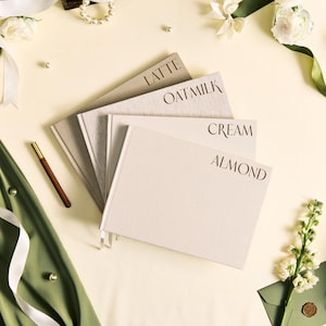 K&ouml;nnte beinhalten: Vier Notizb&uuml;cher mit den W&ouml;rtern "LATTE", "OATMILK", "CREAM" und "ALMOND" auf den Einb&auml;nden. Die Notizb&uuml;cher sind in Beige- und Cremet&ouml;nen gehalten. Ein goldfarbener Stift und eine Perlenkette sind ebenfalls zu sehen.