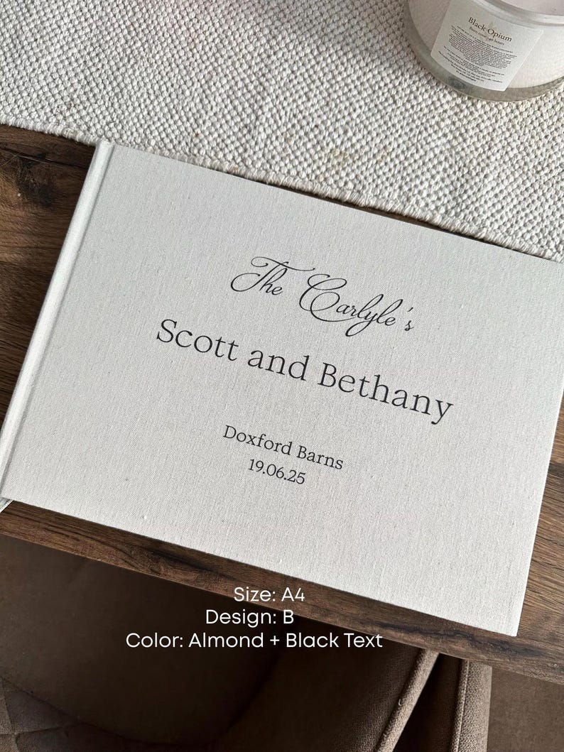 K&ouml;nnte beinhalten: Ein wei&szlig;es G&auml;stebuch im A4-Format mit schwarzem Text. Auf dem Einband steht "The Carlyle's Scott and Bethany" mit "Doxford Barns 19.06.25" darunter. Das Design ist B, mit mandelfarbener Farbe und schwarzem Text.