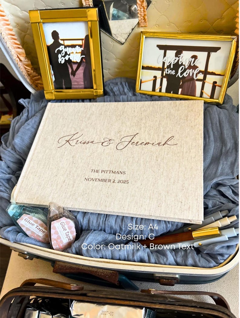 K&ouml;nnte beinhalten: Eine Hochzeits-Themenausstellung mit einem Fotoalbum, zwei gerahmten Fotos und zwei Rollen Klebeband. Das Album ist cremefarben mit braunem Text "Krissa & Jeremiah" und "The Pittmans, November 2, 2025."