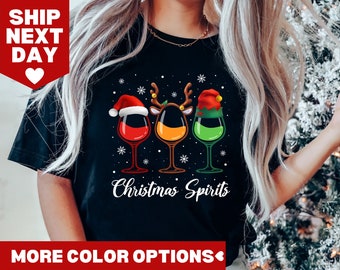 May include: Black t-shirt with a Christmas-themed design featuring three wine glasses with Santa, reindeer, and elf hats. The text "Christmas Spirits" is printed below the glasses.
