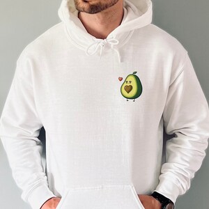 May include: A white hoodie with a small avocado design on the front. The avocado has a heart in the middle and a small red heart above it.