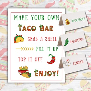 May include: A white sign with red border and text "MAKE YOUR OWN TACO BAR" with illustrations of tacos, peppers, and chips. Includes tent cards labeled "AVOCADOES", "JALAPEÑOS", and "CHICKEN".