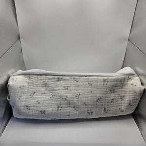 May include: A white, rectangular pencil case with a floral pattern of small blue and green flowers. The case has a zipper closure and is made of a crinkled fabric.