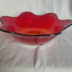 May include: A large, red glass bowl with a wavy rim. The bowl is made of clear glass with a red tint and has a slight amber hue at the bottom.