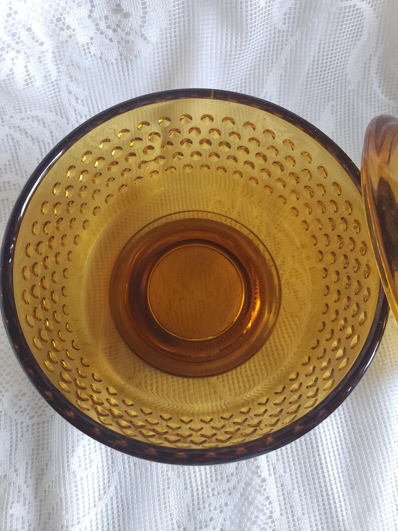May include: Amber-colored glass bowl with a textured, dimpled interior. The bowl has a dark brown rim and a circular base. The design features a series of small, evenly spaced indentations across the surface.