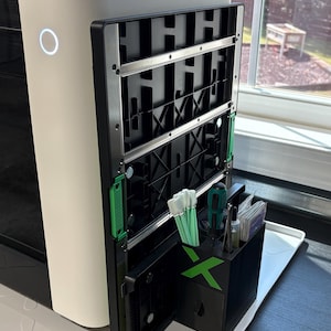 May include: A white and black 3D printer enclosure featuring a side-mounted black storage organizer with a green X logo. The organizer holds green-tipped cleaning swabs, a screwdriver, tweezers, and small packets of accessories.