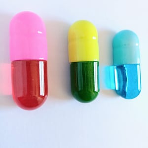 May include: Three colorful, capsule-shaped objects. One is pink and red, another is yellow and green, and the third is blue and turquoise. The objects are on a white background.