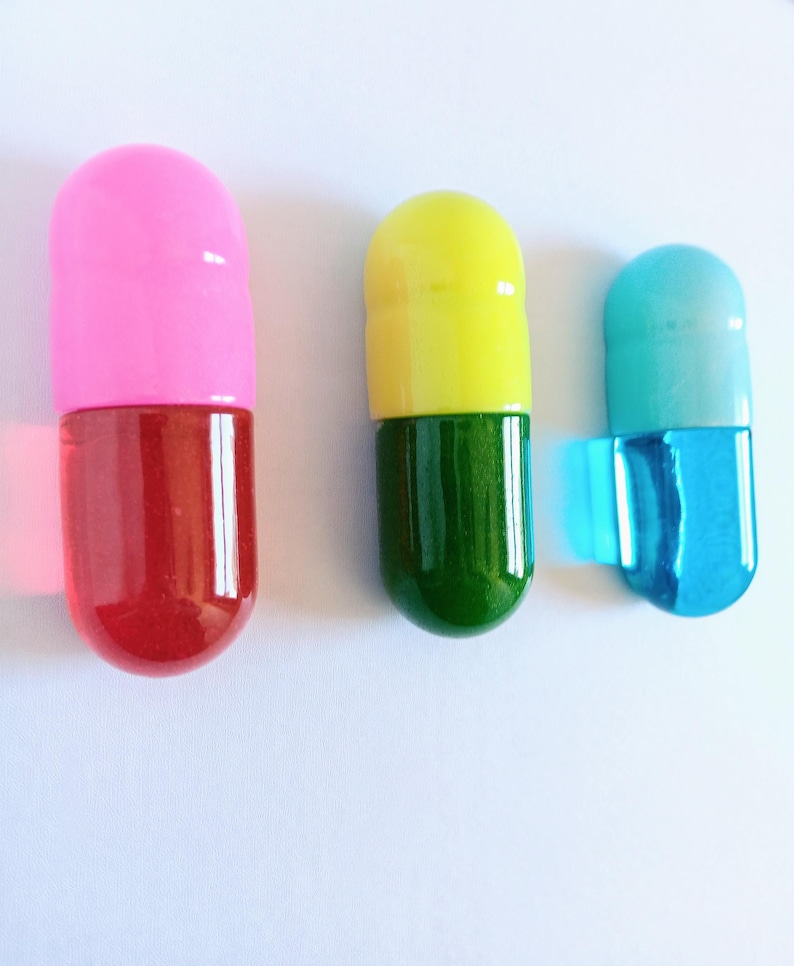 May include: Three colorful, capsule-shaped objects. One is pink and red, another is yellow and green, and the third is blue and turquoise. The objects are on a white background.