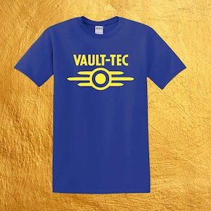 May include: A blue t-shirt with the text "VAULT-TEC" in yellow, along with a yellow emblem. The shirt is displayed against a textured gold background. The t-shirt is a crew neck style.