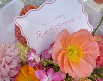 May include: A bouquet of pink, orange, and yellow flowers with a white card that says "Will you be my Maid of Honour?"