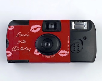 Puede incluir: Cámara desechable roja con el texto "Lara's 30th Birthday" y labios rosas impresos en la parte delantera. La cámara tiene un flash negro y una ventana de fecha que dice "Diciembre 2024".