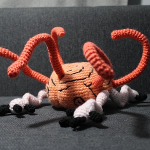 Op de afbeelding: Een gehaakt pluche speelgoed in de vorm van een brein met meerdere oranje tentakels. De hersenen zijn roze en hebben een zwarte lijn erop getekend.
