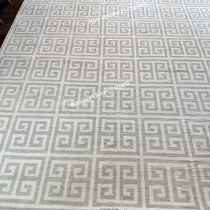 May include: A rectangular rug with a repeating geometric pattern in light gray and white. The rug has a fringed edge and the text "Noor Handsome Carpets" is visible on the rug.